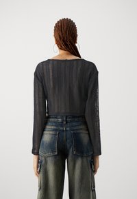 Crochet navy long-sleeve top with a loose fit, featuring a wide neckline and textured pattern. Paired with high-waisted denim cargo pants.