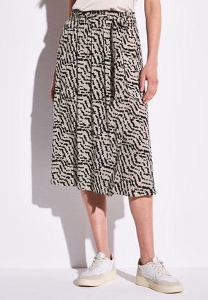 Beige skirt with black abstract pattern, pleated design, and an elastic waistband. Paired with white and beige sneakers.