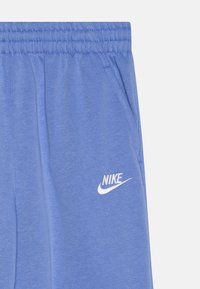 Svetlo modre Nike trenirka narejene iz mehke tkanine, z elastičnim pasom, stranskimi žepi in belim logotipom na levi stegnu.