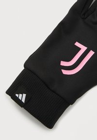 Gant de sport noir avec une manchette à côtes. Présente un logo rose et une petite étiquette noire avec un motif triangulaire blanc. Texture de matériau douce.