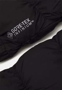 Schwarze isolierte Jacke mit GORE-TEX INFINIUM™-Logo, glatter Textur, gestepptem Design und leicht glänzender Oberfläche.