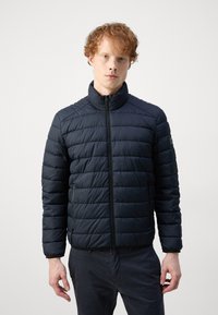 Navy puffer jacket with a high collar. Horizontal quilted design, front zipper, and side pockets. Soft, lightweight material.