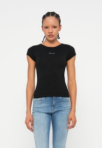 Tricou negru, mulat, cu mâneci scurte, guler rotund și un mic logo alb pe piept. Asortat cu blugi albaștri din denim.