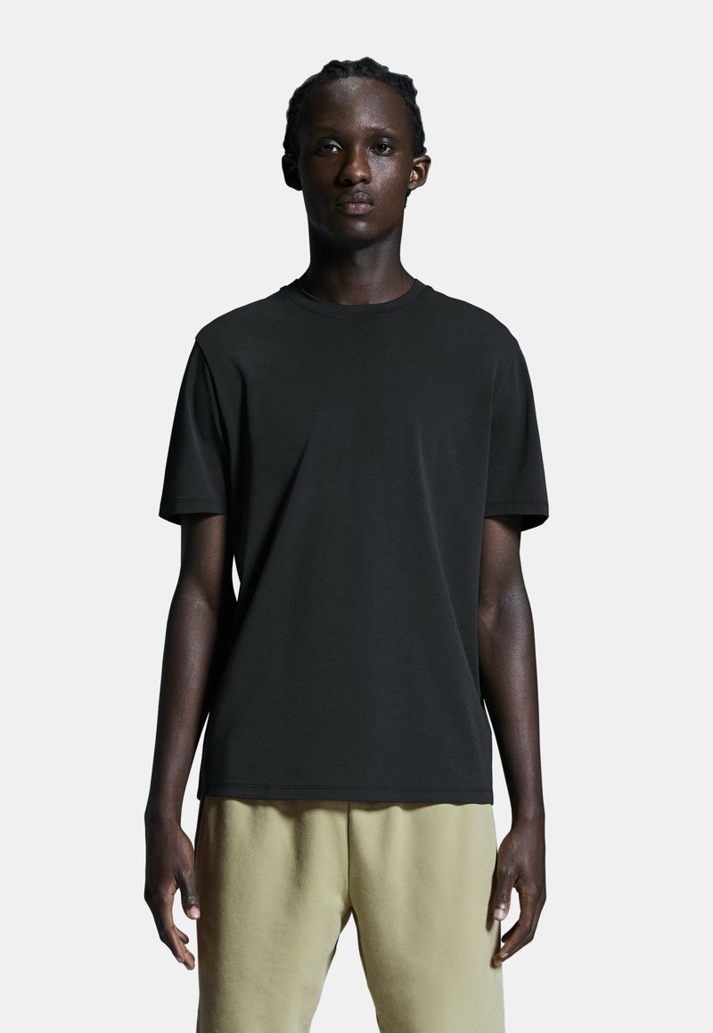 Sort bomulds T-shirt med rund hals og korte ærmer, som har en glat tekstur. Bæres med lyse joggers.