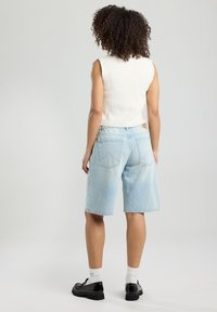 Vaaleansiniset farkkushortsit, joissa on väljä istuvuus ja karkea helma. Yhdistetty valkoiseen hihattomaan neulepaitaan ja mustiin kenkiin, esittelee rentoa tyyliä.