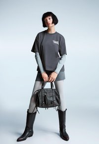 Tricou oversized gri, purtat peste o bluză cu mânecă lungă gri deschis, asortat cu o fustă gri și colanți gri deschis. Bocanci negri până la genunchi și o geantă neagră texturată.