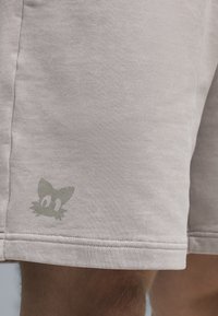Light gray shorts made of soft fabric featuring a small green cat graphic on the lower hem, with simple stitching details.