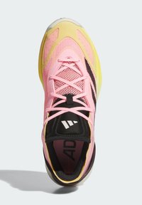 Sportssko med en pink mesh overdel, gule detaljer, sorte snørebånd og et signaturlogo. Formet sål med en gennemsigtig bund.
