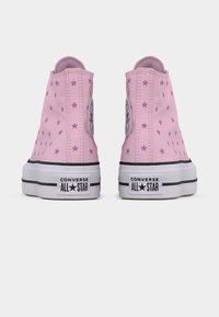 Ροζ καμβά ψηλοτάκουνα αθλητικά παπούτσια με διάσπαρτα σχέδια αστεριών, λευκή λαστιχένια σόλα και μαύρες ρίγες. Διαθέτουν το λογότυπο Converse στην πλευρά.