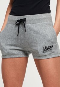 Pantalones cortos deportivos gris de mezcla de algodón con una cinturilla elástica, cordón negro, bolsillos laterales y el logotipo "SUPERDRY SPORT" en negro.