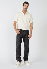 Schwarze Lederhosen mit entspannter Passform, kombiniert mit einem hellcremefarbenen Poloshirt. Das Outfit wird mit cremefarbenen Sneakers mit grauen Akzenten abgerundet.