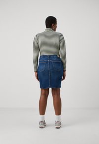 Saia lápis de ganga de cintura alta, combinada com um suéter de gola alta às riscas preto e branco. Apresenta bolsos e uma textura suave.