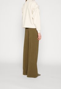 Beige sweatshirt med puffärmar och knappaccenter, tillsammans med vida olivgröna byxor, båda gjorda av mjukt, texturerat tyg.