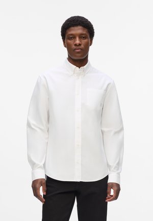 Weißes Langarmhemd aus Baumwolle mit Button-Down-Kragen und einer Brusttasche. Glatte Textur mit klassischer Passform, kombiniert mit schwarzen Hosen.