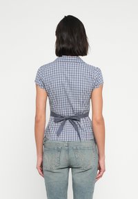 Μπλούζα με κοντό μανίκι, καρό σε ναυτικό μπλε και άσπρο, με εφαρμοστή μέση και ζώνη για δέσιμο στο πίσω μέρος· τζιν παντελόνι με διακοσμητικά ράμματα στις πίσω τσέπες.