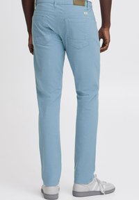 Lichtblauwe slim-fit broek met achterzakken en een soepele textuur. Gecombineerd met grijze sneakers, wat een casual, moderne uitstraling geeft.