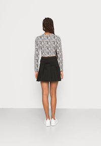 Saia preta plissada combinada com uma blusa de manga longa com padrão de zebra. O tecido parece liso e o conjunto é complementado com ténis brancos.