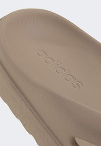 Svetlohnedé adidas šľapky so štruktúrovanou stielkou a jemným logom. Podrážka má mierne drsný vzor pre lepšiu priľnavosť.