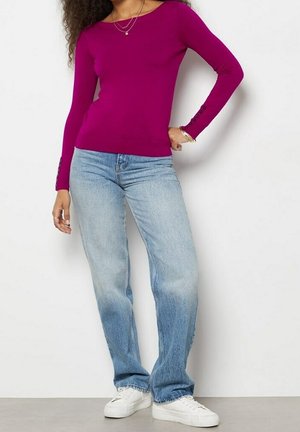 Aansluitend magenta langslavend shirt met knoopaccenten bij de mouwen, gecombineerd met lichtblauwe rechtgesneden jeans en witte sneakers.