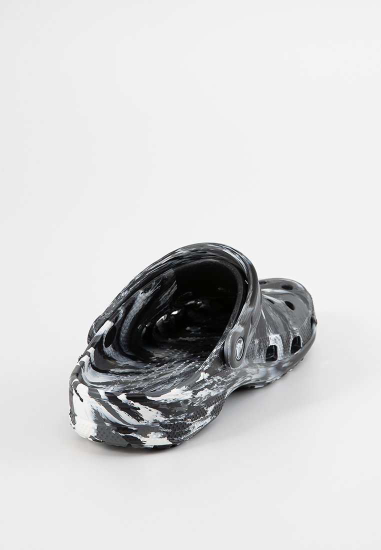 Sabots marbrés noir et blanc avec une forme arrondie, fabriqués en matériau léger. Comprend des trous de ventilation et une sangle au talon.