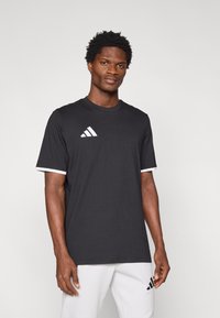 Μαύρο κοντομάνικο μπλουζάκι με λευκές λεπτομέρειες στα μανίκια και λευκό λογότυπο Adidas στο στήθος. Μαλακό ύφασμα, άνετη εφαρμογή.