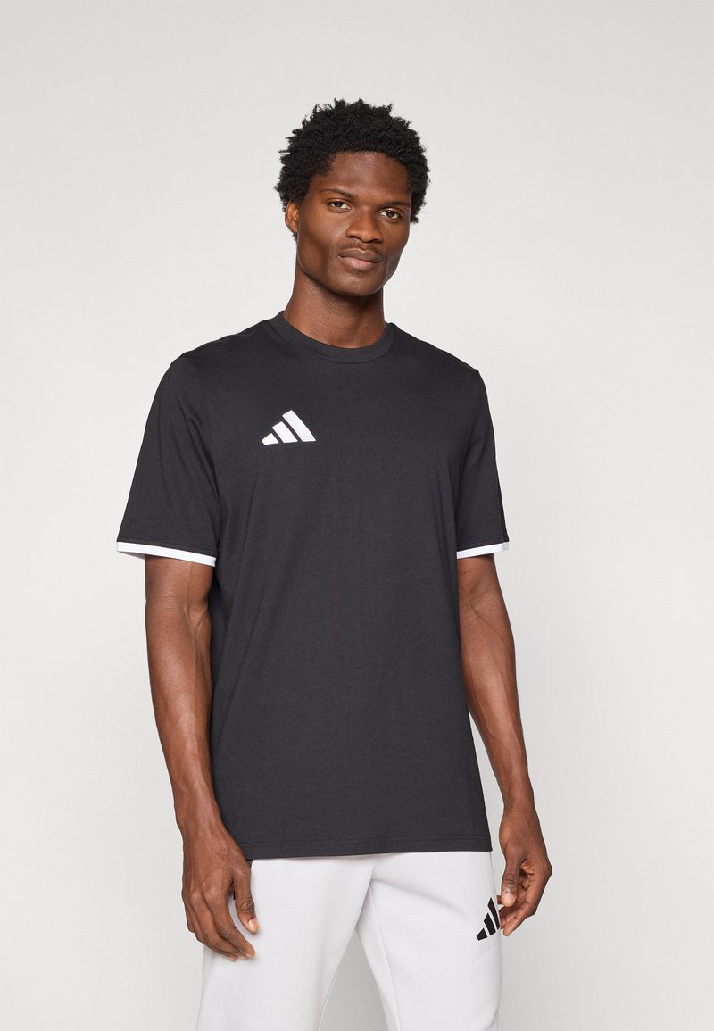 Μαύρο κοντομάνικο μπλουζάκι με λευκές λεπτομέρειες στα μανίκια και λευκό λογότυπο Adidas στο στήθος. Μαλακό ύφασμα, άνετη εφαρμογή.