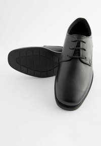 Chaussures habillées en cuir noir avec une finition lisse, bout arrondi, système de laçage et semelle en caoutchouc texturée présentant un motif en grille.