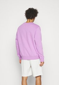 Jasnofioletowa bluza z prążkowanymi mankietami i obrębem, z okrągłym dekoltem. Noszona z białymi szortami, o luźnym kroju.