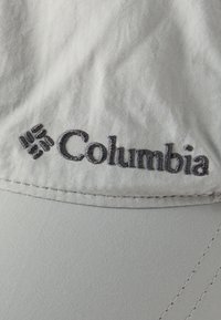 Ανοιχτό γκρι ύφασμα με μαύρο κεντημένο λογότυπο και σύμβολο της Columbia, που δείχνει ραμμένη ραφή και ομαλή υφή.