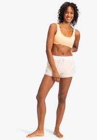 Licht perzikkleurige sportbeha en doorschijnende witte shorts met een elastische tailleband. Het ontwerp is eenvoudig, met een gladde textuur en minimale details.