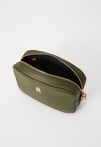 Olive green leather cosmetic bag with a gold zipper, rounded shape, and a small logo on the front. Interior features a dark lining.