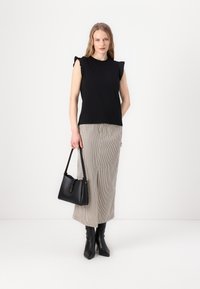Schwarzes ärmelloses Top mit gerafften Schulterdetails, kombiniert mit einem gestreiften langen Rock. Das Model hält eine schwarze Handtasche und trägt spitze Stiefeletten.