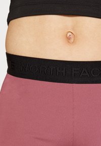 Czarny elastyczny pas z logo "THE NORTH FACE", połączony z dopasowanym, miękkim różowym materiałem w talii, ukazującym gładką fakturę.