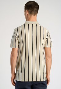 Beżowa koszula z krótkim rękawem w czarne pionowe paski, z klasycznym kołnierzykiem i gładką teksturą. Tylny widok ukazuje czyste szwy i dopasowanie.