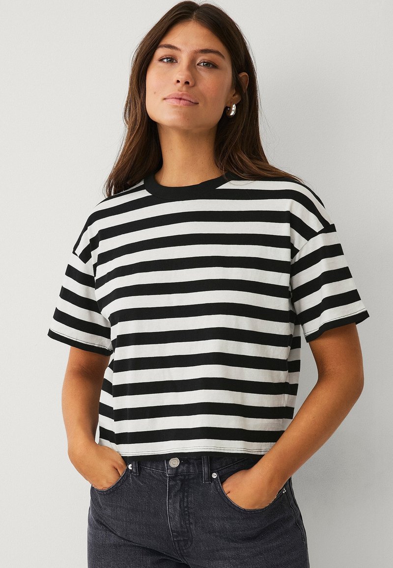T-shirt court noir et blanc à rayures avec un col rond et des manches courtes, fabriqué à partir d'un tissu lisse. Présente une coupe décontractée.