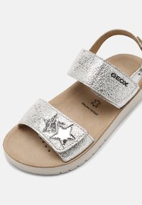 Silver patentläder sandalett med två justerbara remmar, stjärnformade detaljer och en vadderad beige innersula med luftflödesperforeringar.