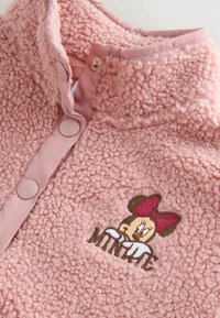 Weicher, rosa Fleece-Pullover mit Kragen, ausgestattet mit cremefarbenen Knöpfen, strukturiertem Stoff und einer gestickten Figur mit einer roten Schleife.