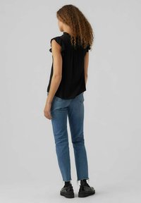 Blusa nera con maniche corte a volants, dettaglio della piega sul retro, abbinata a jeans di denim blu medio e scarpe platform nere con suola spessa.