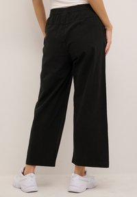 Black, wide-leg pants made of lightweight fabric. Features an elastic waistband and stitched seams, paired with white athletic shoes.