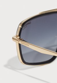 Ochelari de soare din metal auriu cu lentile mari, pătrate. Nuanta gradient este gri închis; rama are un design cu dungi. Gravură "CARRERA" pe braț.