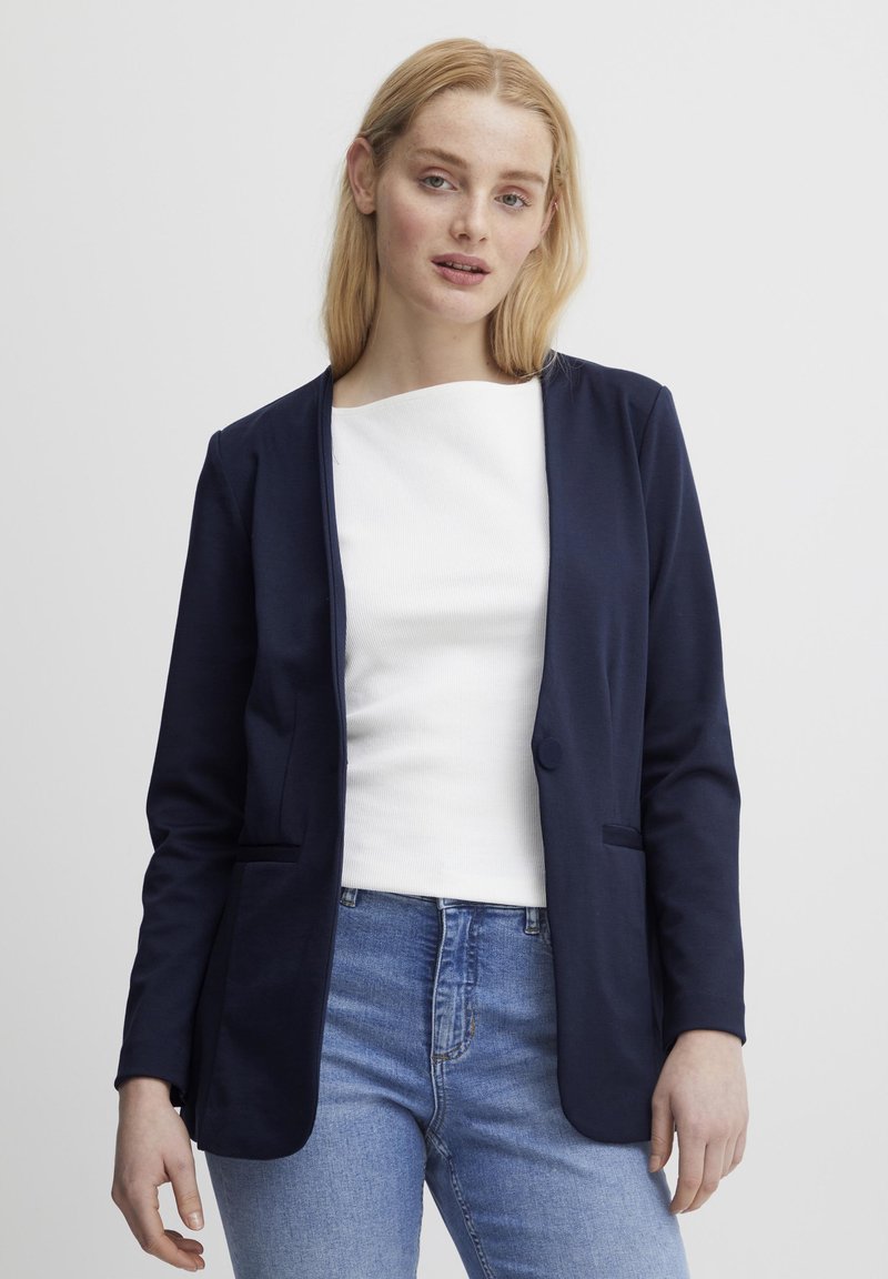 Navyblauwe blazer van een zachte stof, met een geknipt kraag, enkele knoopsluiting en twee voorkruiszakken. Gekocht over een witte top.