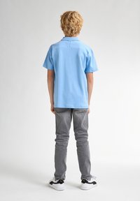 Ljusblå kortärmad polo skjorta i bomull, med klassisk krage, ihop med grå slim fit-jeans och sneakers med svarta detaljer.