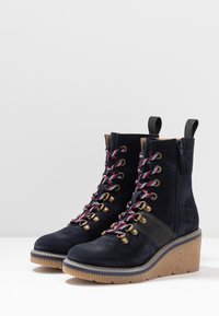 Botas de tobillo de ante azul marino con un acento marrón, que cuentan con ojales dorados, cordones rojos y azules, y una suela de plataforma Beige texturizada.