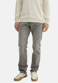 Szürke, slim fit farmernadrág, amely finom textúrával rendelkezik. Alacsony szárú, fehér sportcipővel párosítva, bézs részletekkel.