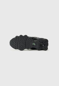 Black sneaker sole featuring textured rubber with various grip patterns, rounded shapes, and a green accent. Smooth surface overall.