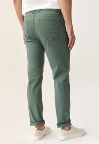 Chinos de algodón verdes con un corte slim, con puños enrollados, dos bolsillos traseros y sutilezas en las costuras. Combinados con zapatillas blancas.