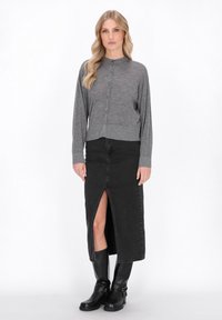 Grijze button-up cardigan met lange mouwen, gecombineerd met een zwarte denimrok met een split aan de voorkant, en zwarte kniehoge laarzen.