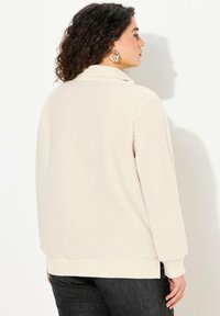 Giacca in tessuto morbido e soffice color crema, con una vestibilità rilassata, orlo e polsini a coste, e colletto pieghevole. Senza chiusure visibili o motivi.