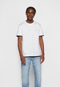 T-shirt in cotone bianco con polsini e orlo a coste neri. Piccolo logo 'CK' sul petto. Vestibilità rilassata, scollatura rotonda. Jeans in denim blu chiaro.