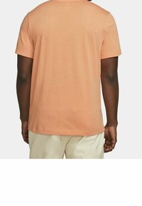 Kortärmad t-shirt i ljus persikofärg, gjord av mjukt tyg, med avslappnad passform och rak nederkant. Har en enkel design utan dekorationer.